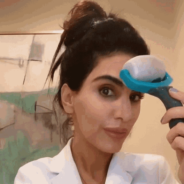 a woman in a white coat is holding an ice roller in front of her face .