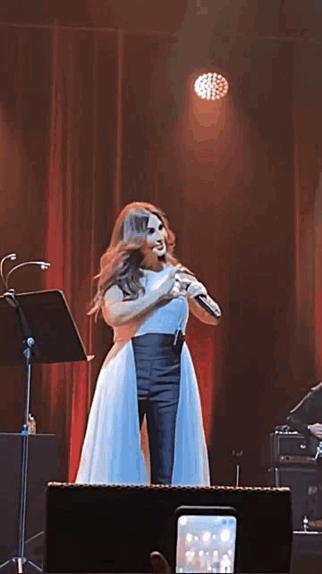 a woman in a white dress singing into a microphone on a stage