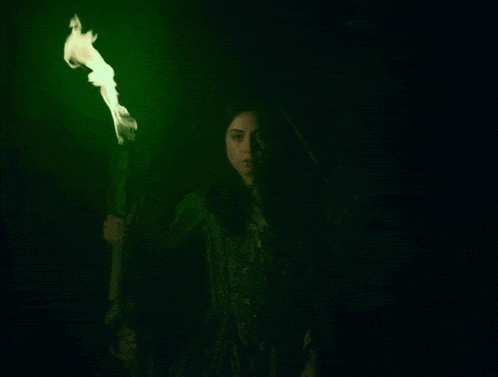 a woman holding a torch in the dark with a green light behind her
