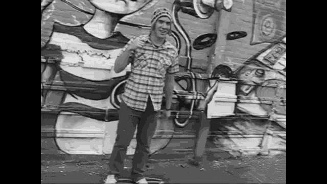 a man in a plaid shirt is standing in front of a graffiti wall