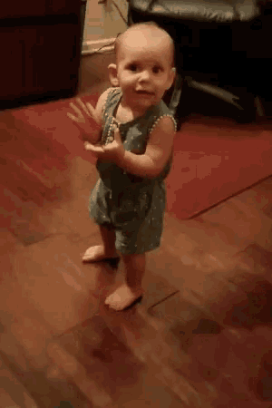 a baby in a blue dress is standing on a wooden floor .