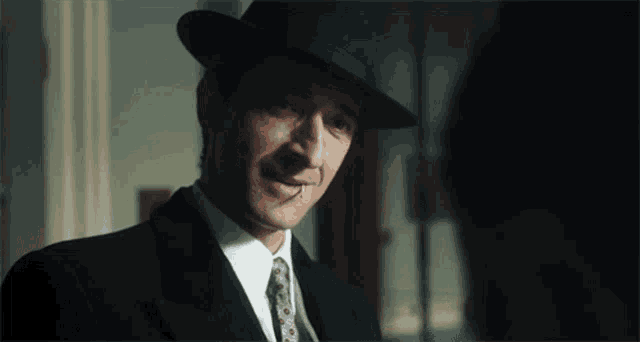 a man with a cigarette in his mouth wearing a suit and hat