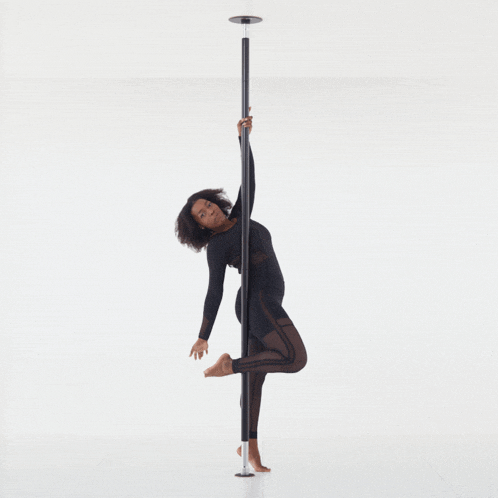 a woman in a black top and black pants is standing on a pole