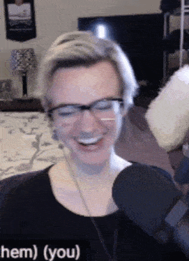 a woman wearing glasses and a black shirt is smiling in front of a microphone with the words hem ( you ) underneath her