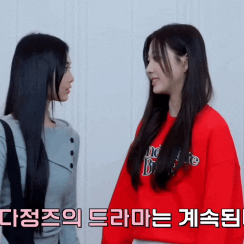 two women are standing next to each other and one of them is wearing a red sweatshirt that says " one bite "