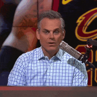 a man in a plaid shirt is sitting in front of a microphone in front of a cleveland cavaliers logo
