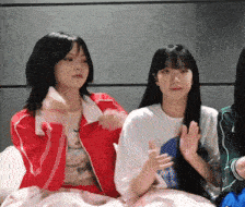 a woman in a red jacket sits next to another woman in a white shirt