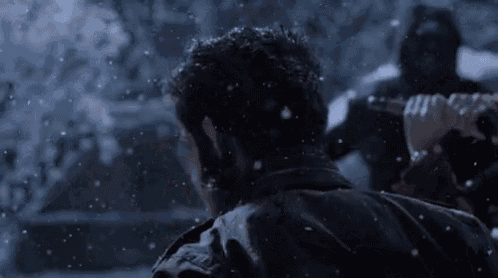 a man in a leather jacket is holding a knife in the snow .