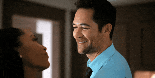 a man in a blue shirt and tie smiles while a woman looks on
