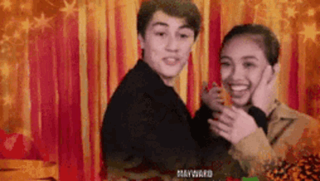 a boy and a girl are standing next to each other in front of a red curtain .
