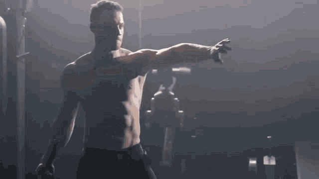 a shirtless man is stretching his arms in a dark gym