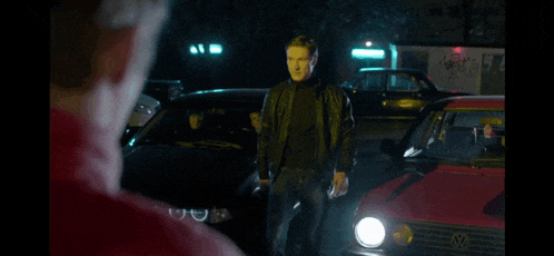 a man in a black leather jacket is standing in front of a red vw golf