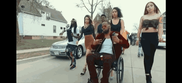 a man in a wheelchair is being pushed down a sidewalk by a group of people