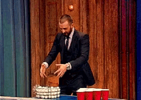 a man in a suit and tie stands in front of a table with red cups