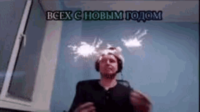 a man wearing headphones and a hat with sparklers on his head is standing in front of a window in a room .