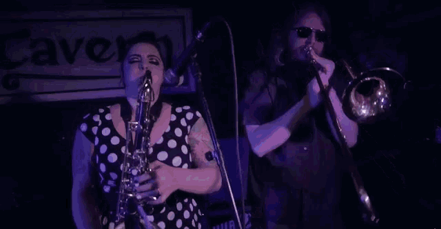 a woman playing a saxophone next to a man playing a trombone in front of a sign that says cave