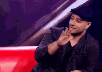a man wearing a hat and a jacket is making a peace sign .