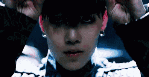 a close up of a person 's face with their hands on their ears and a dark background .