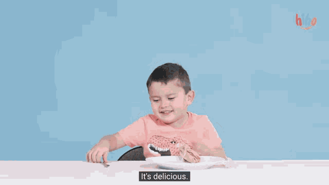 a young boy is sitting at a table eating a sandwich with a fork and knife and says it 's delicious