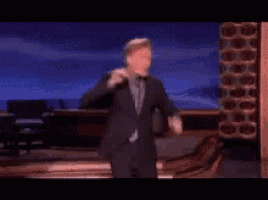 a man in a suit and tie is dancing in front of a blue background