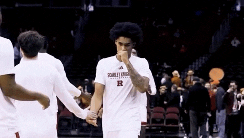 a man in a scarlet knight t-shirt is walking on a basketball court .