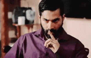 a man with a beard is sitting in a chair with his finger on his mouth .