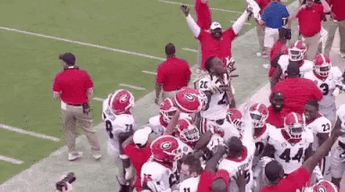 a group of football players are standing on a field with their hands in the air .