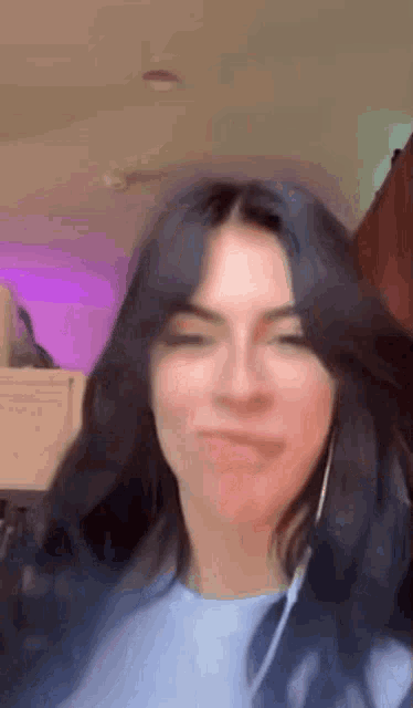 a woman with long black hair is wearing headphones and making a face .
