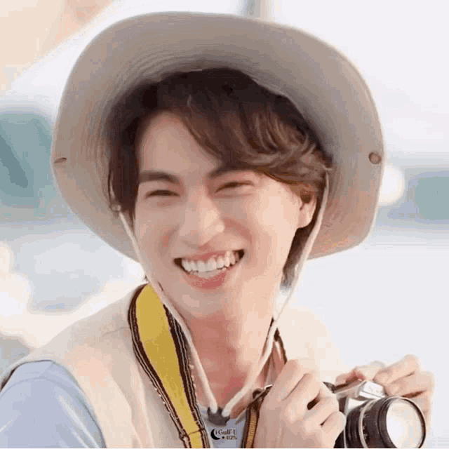 a young man wearing a hat and holding a camera is smiling