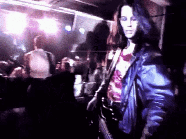 a woman in a blue leather jacket is walking in a crowded room