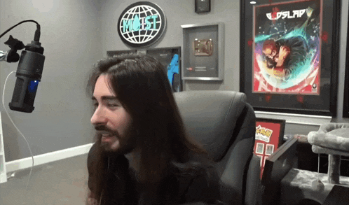 a man with long hair sits in front of a microphone in a room with a sign that says " most "