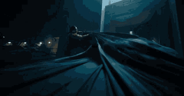 a man stands in front of a black batmobile in a dark room