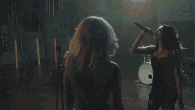 two women standing next to each other in a dark room with a band in the background