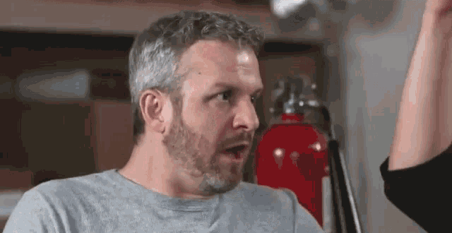 a man with a beard is standing in front of a fire extinguisher and making a funny face .