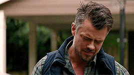 a man with a beard wearing a plaid shirt and a vest is standing in front of a house .