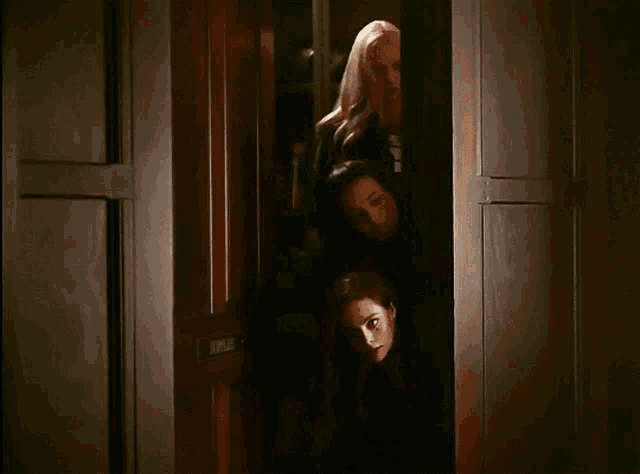 three women peeking out from behind a door that says ' ep ' on it