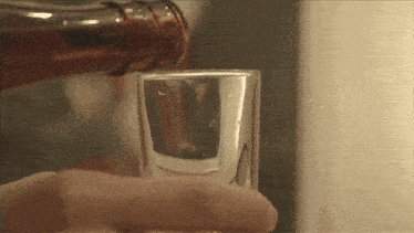 a shot glass is being poured with a brown liquid