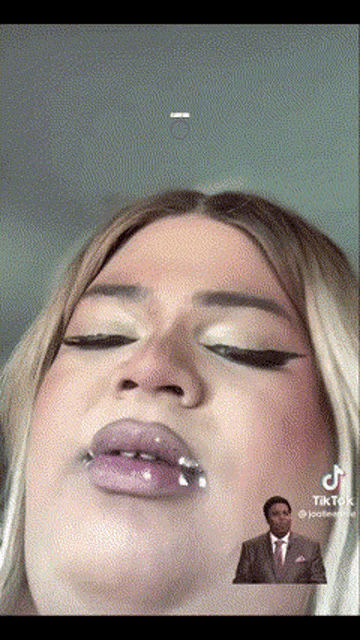 a close up of a woman 's face with a man in a suit behind her