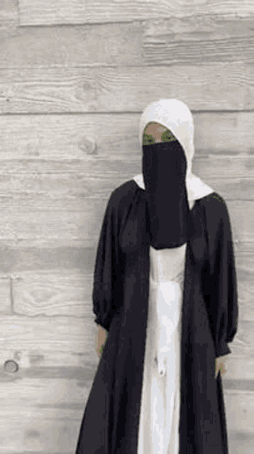 a woman wearing a hijab and a black abaya is standing in front of a wooden wall .