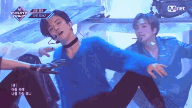 a man in a blue sweater is performing on a stage with a mnet logo behind him
