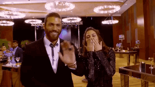 a man and a woman are standing next to each other in a room and the woman is covering her mouth with her hands .