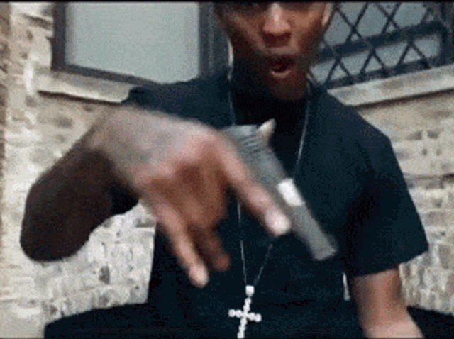 a man with a cross necklace is pointing at a gun .