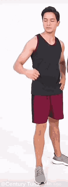 a man in a black tank top and maroon shorts flexes his arm