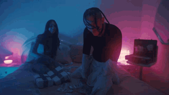 a man and a woman laying on a bed with purple lights behind them