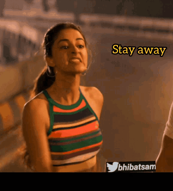 a woman in a striped tank top is standing next to a sign that says stay away