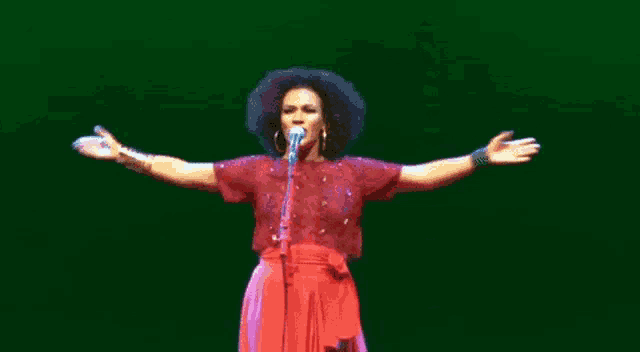 a woman is singing into a microphone with her arms outstretched