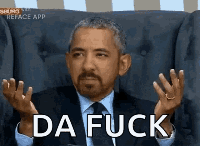 a man in a suit and tie is sitting in a chair making a funny face and saying `` da fuck '' .