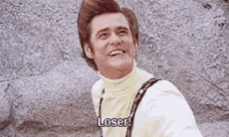 a man in a yellow turtleneck and suspenders is standing in front of a rock wall and smiling .