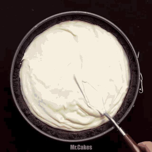 a person is using a spatula to spread white frosting in a pan that says mr. cakes on the bottom