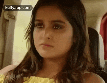 a young girl is sitting in the back seat of a car and making a funny face .